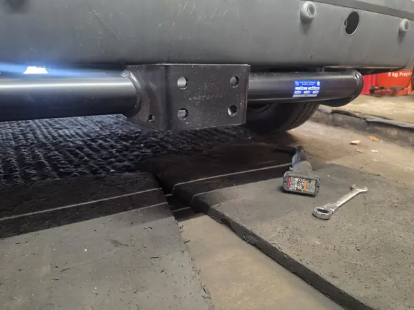 Tow bar mounting plate bolted under a 2008 Ford Transit Connect before the tow ball is fitted, at Village Motor Center in Warrington